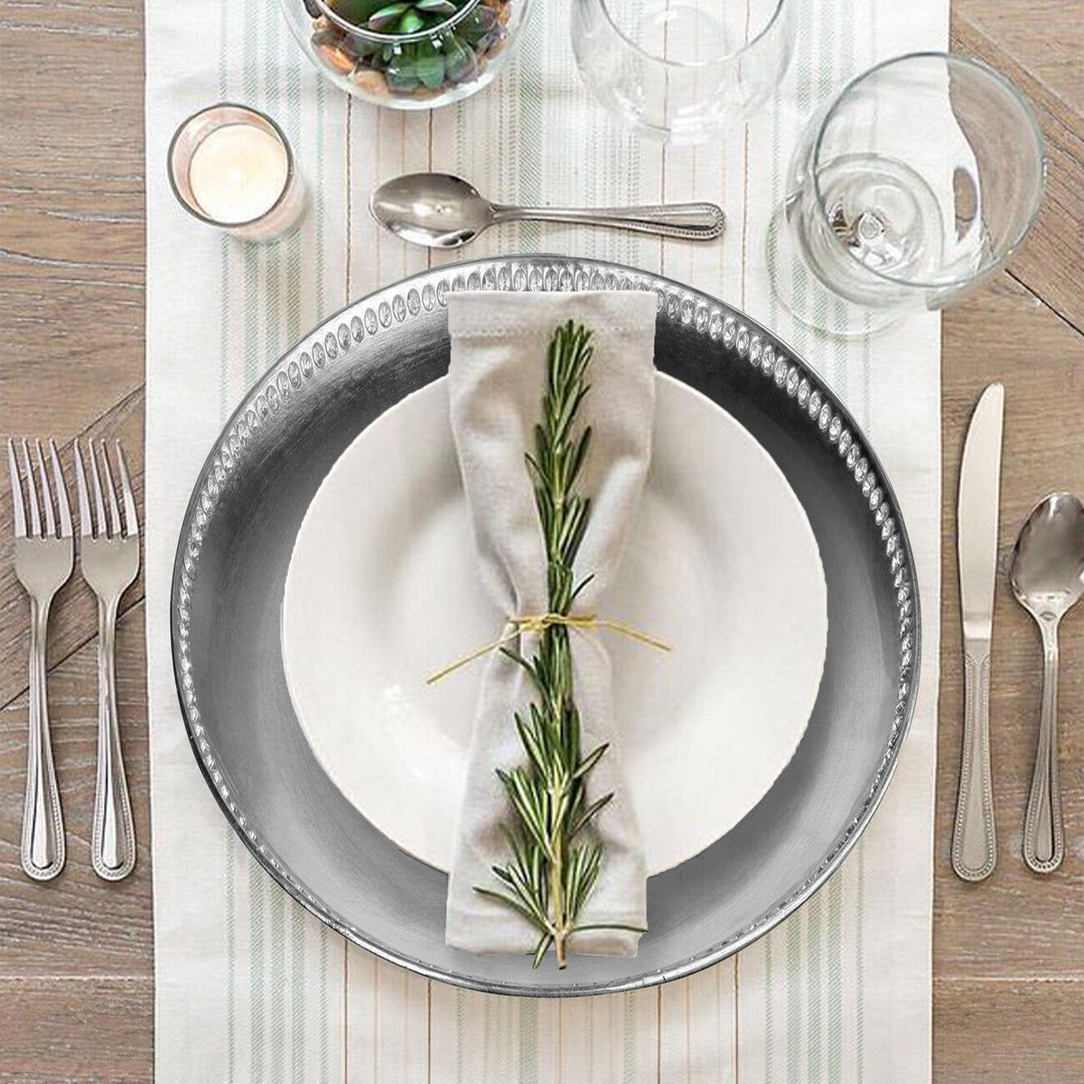 Elegant table setting with gray plates, silverware, and a sprig of rosemary on a white napkin.