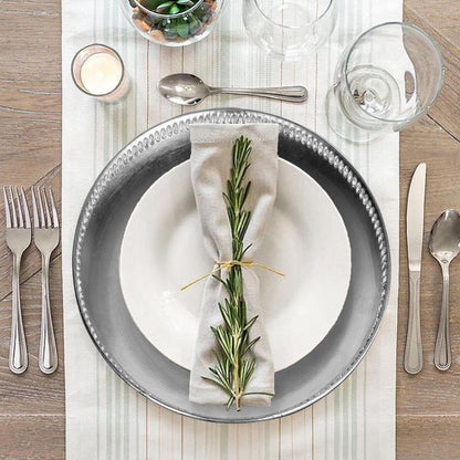 Elegant table setting with gray plates, silverware, and a sprig of rosemary on a white napkin.