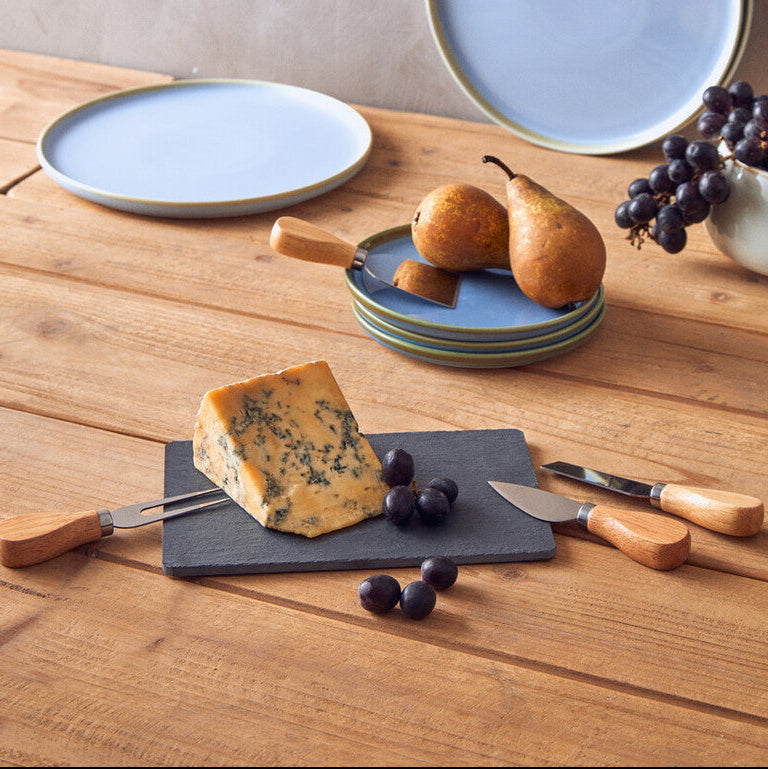 Set of blue ceramic plates on a wooden surface with fruit and cheese.