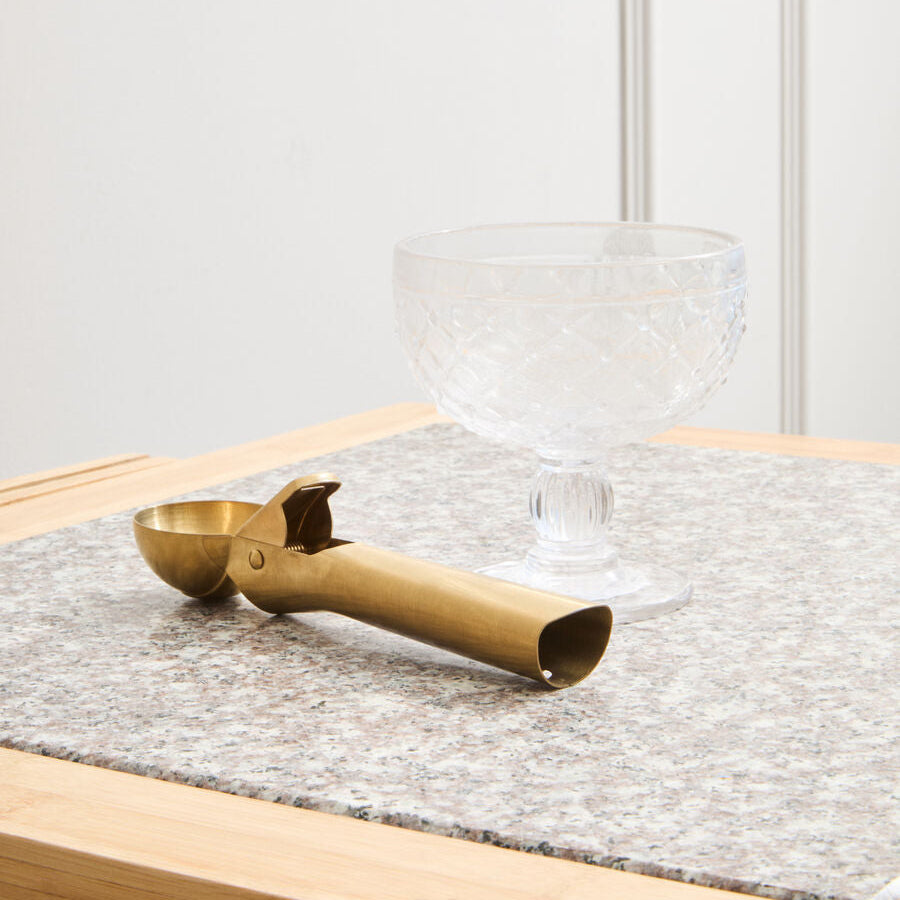 Brass tea scoop on a gray cloth with a glass bowl in the background