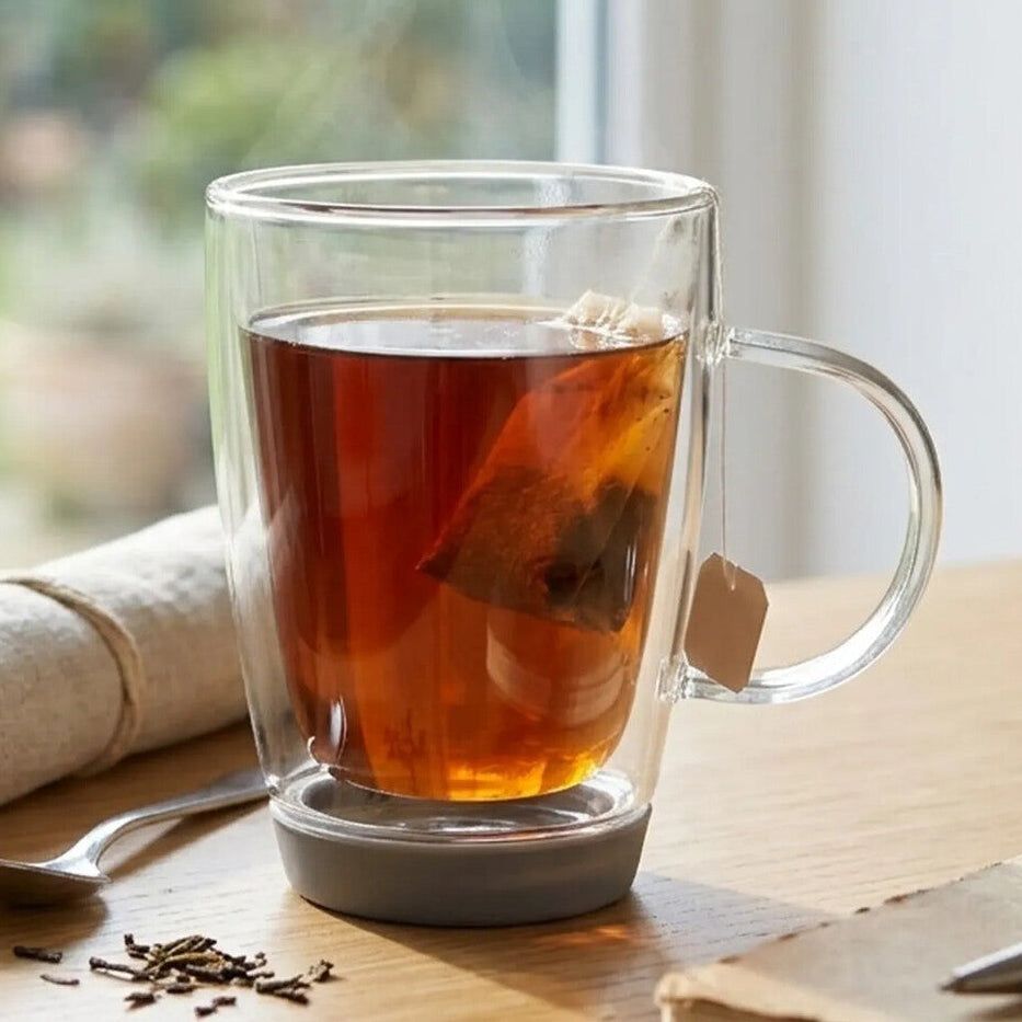 Double-walled glass mug with tea on a wooden surface near a window