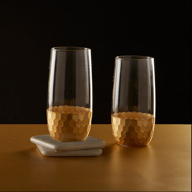 Two glass tumblers with a textured base on a wooden surface against a black background