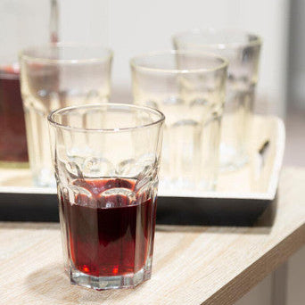 Clear glass with red liquid on a light-colored surface, with a bottle and additional glasses in the background.