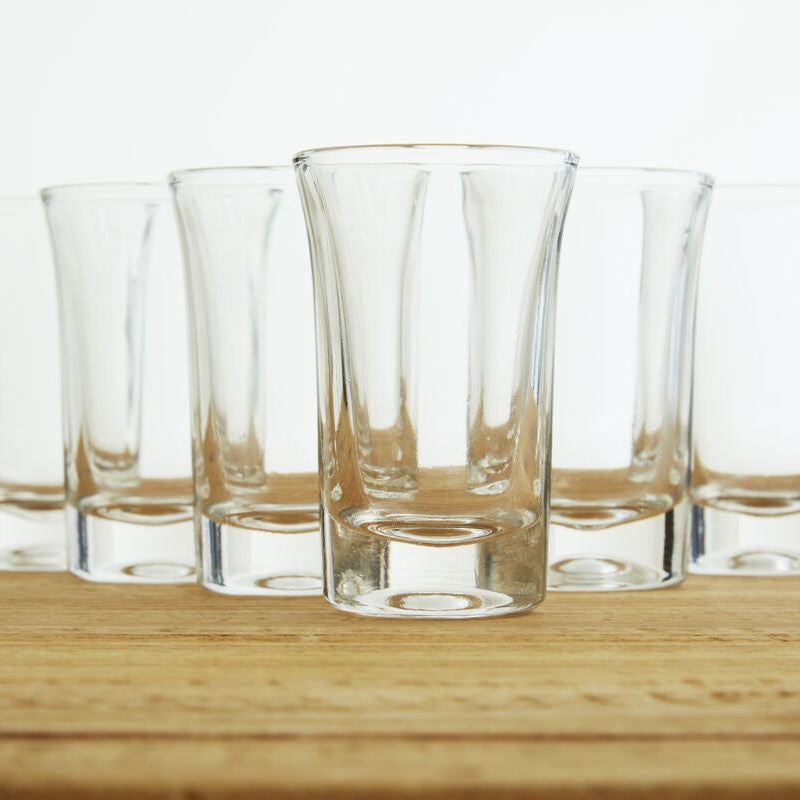 Set of six clear glasses on a wooden surface with a white background