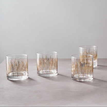 Set of four clear glass tumblers with gold interior patterns on a light gray surface.