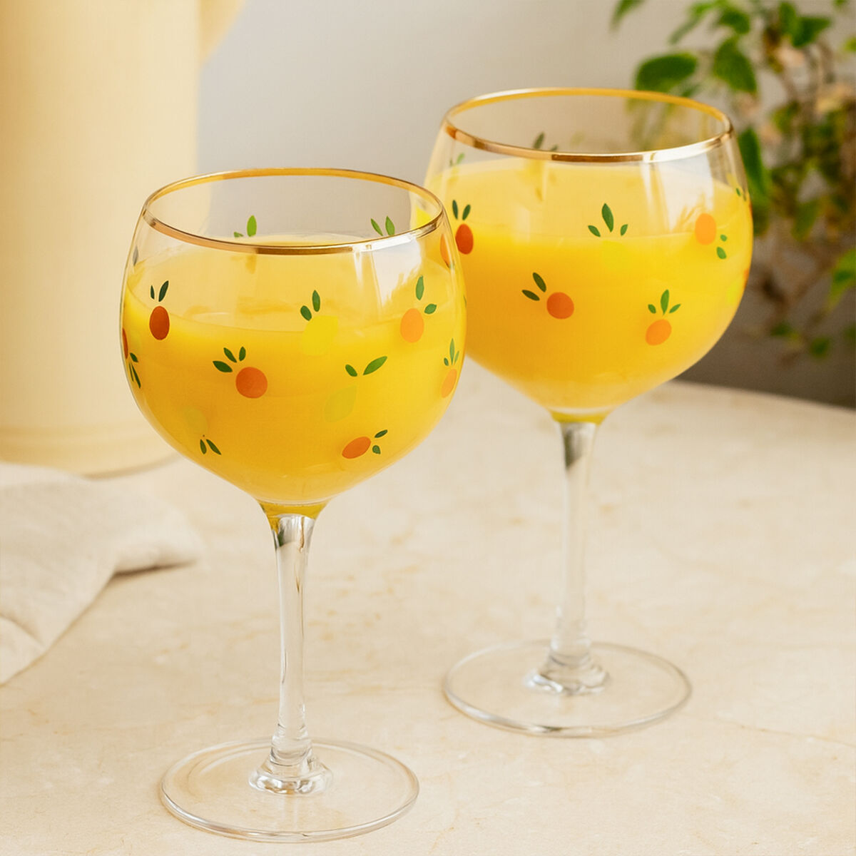 Two wine glasses filled with a yellow beverage on a light surface.