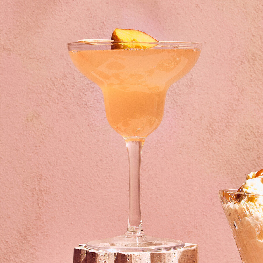 Cocktail in a martini glass with a lemon twist on a pink background