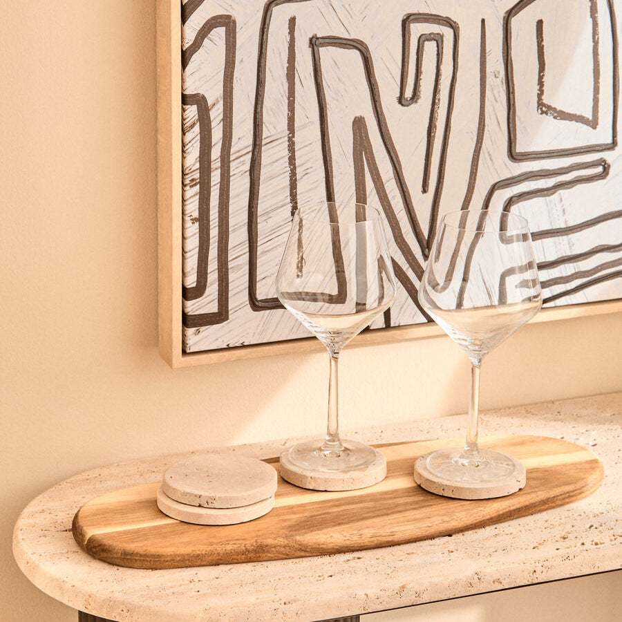 Two wine glasses on a wooden tray with abstract art in the background.