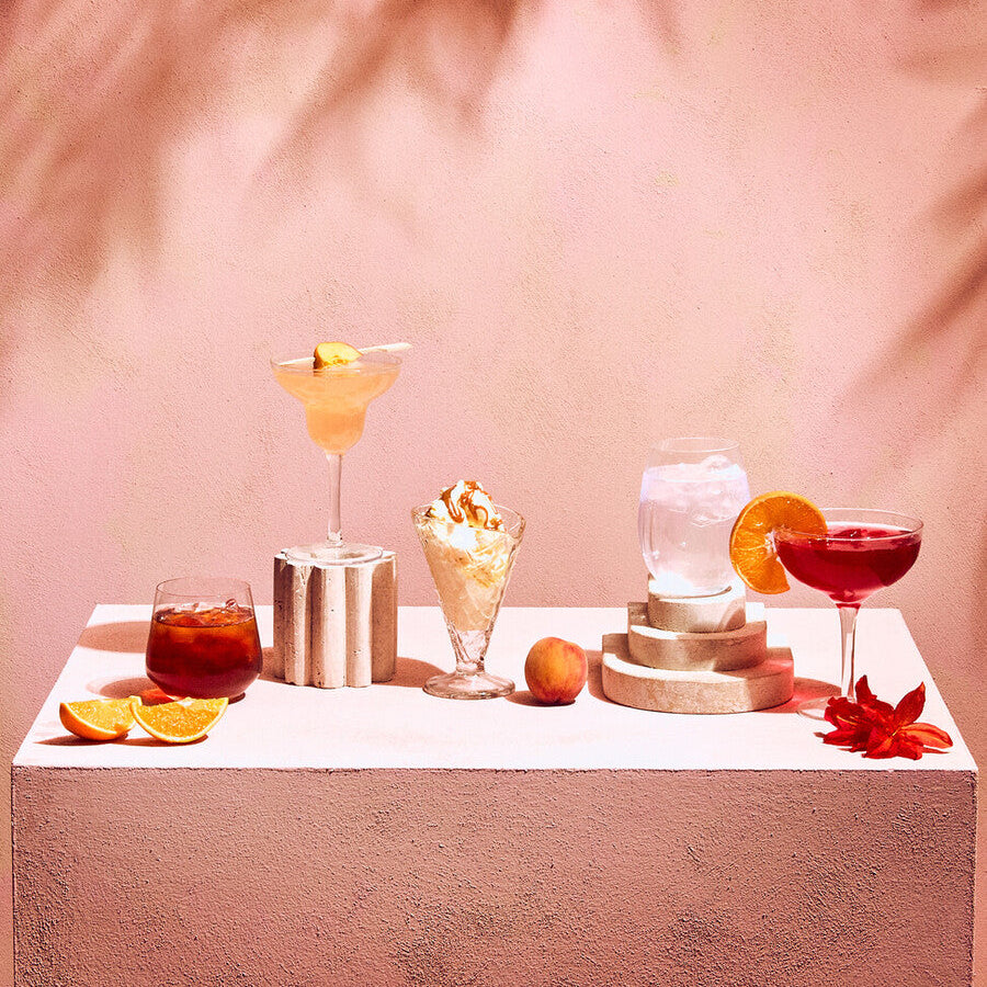 Assorted cocktails on a white surface with a pink background