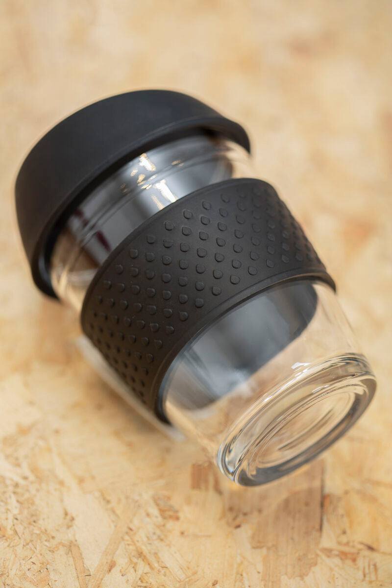 Glass tumbler with black silicone sleeve on a beige surface