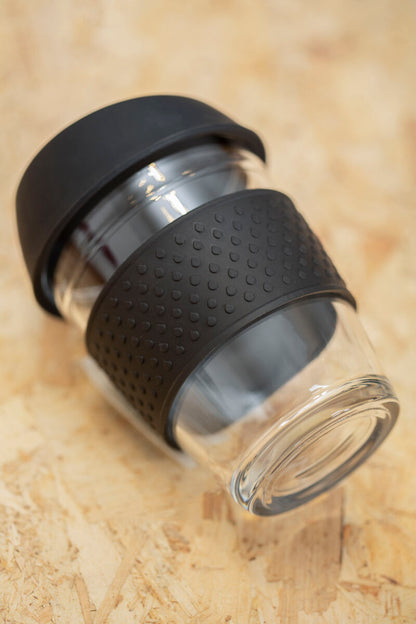 Glass tumbler with black silicone sleeve on a beige surface
