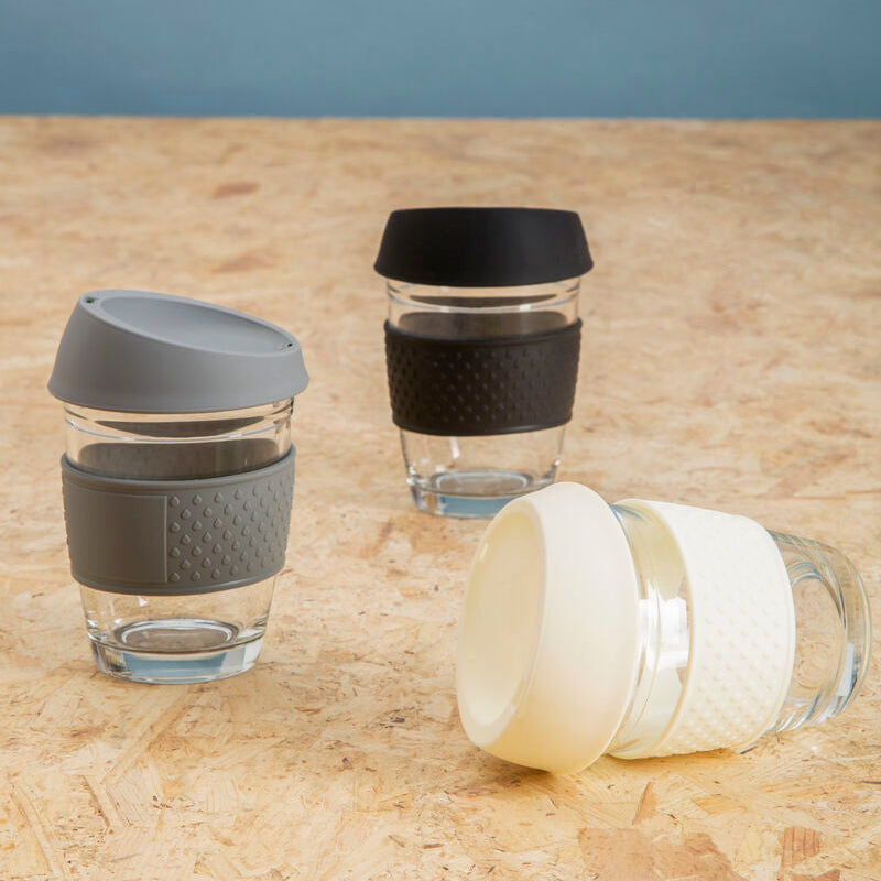 Three reusable coffee cups with different colored lids on a wooden surface.