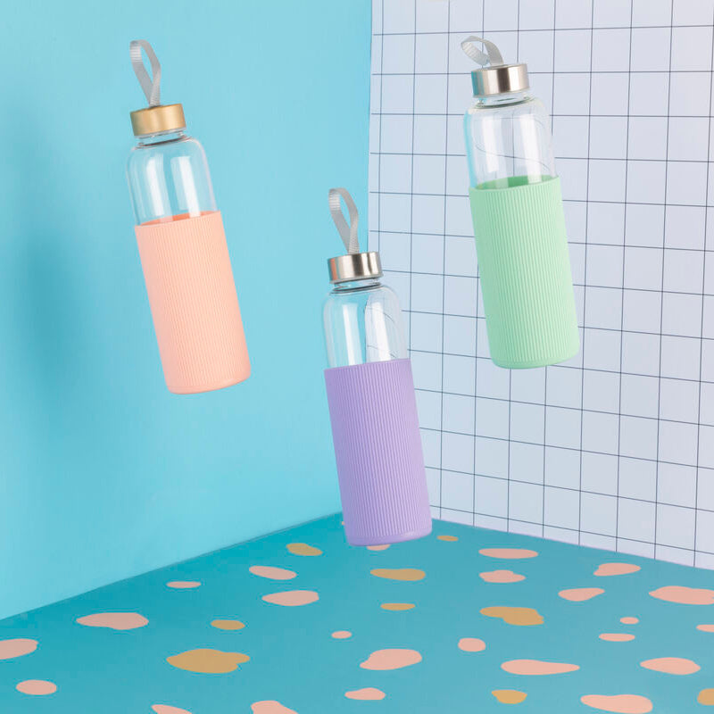 Three glass bottles with colorful silicone sleeves on a polka dot surface with a grid-patterned wall.