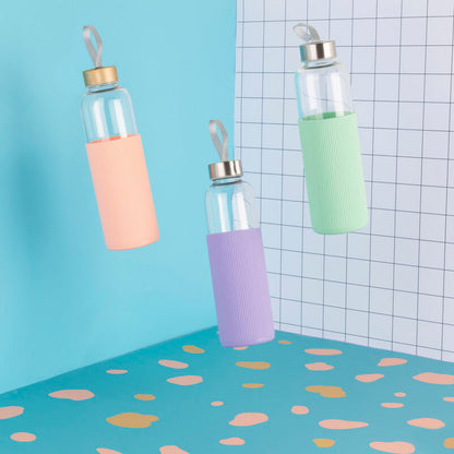 Three glass bottles with colorful silicone sleeves on a polka dot surface with a grid-patterned wall.