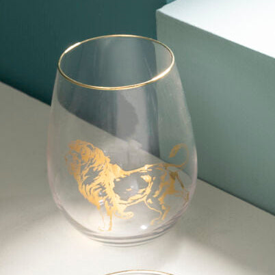Four clear glasses with gold animal illustrations on a light surface against a teal wall.