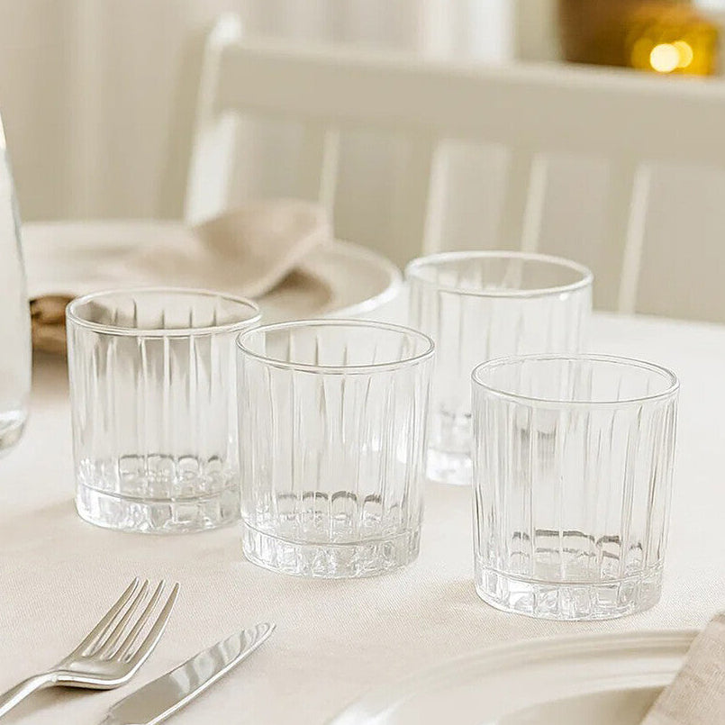 Clear glass tumblers and a carafe on a white tablecloth with a neutral background