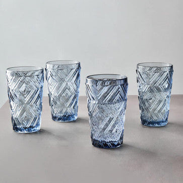 Four blue glass tumblers with geometric patterns on a light gray background