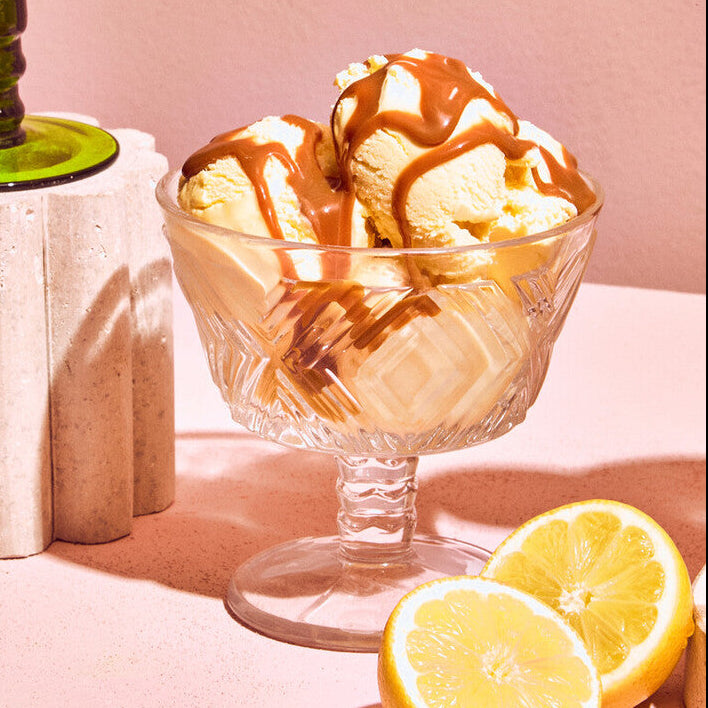 Glass bowl of ice cream with caramel drizzle next to a halved lemon on a pink background
