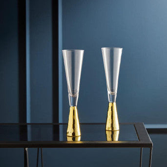 Two clear glasses with gold bases on a dark surface against a blue background