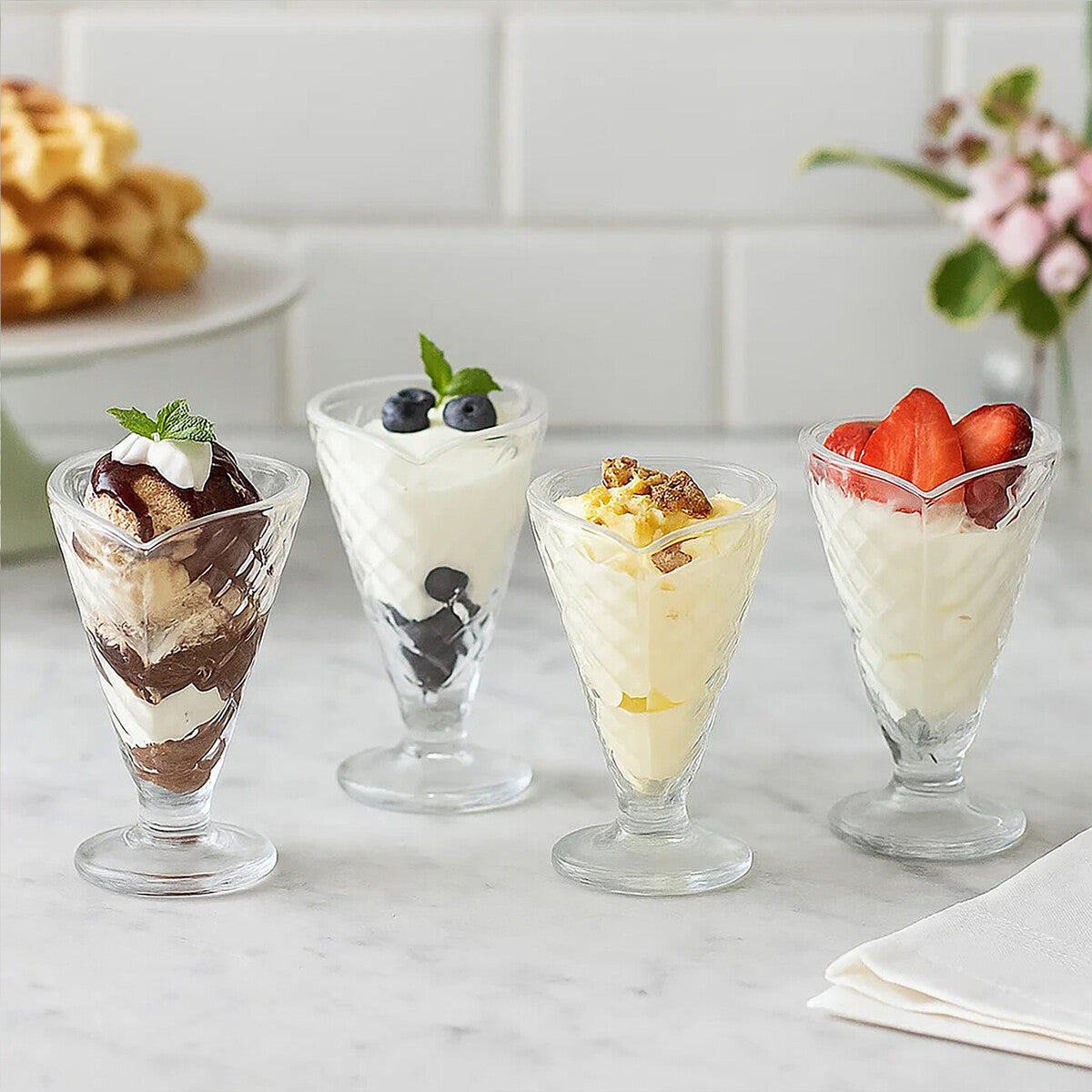 Four glass dessert cups with various desserts on a marble surface.