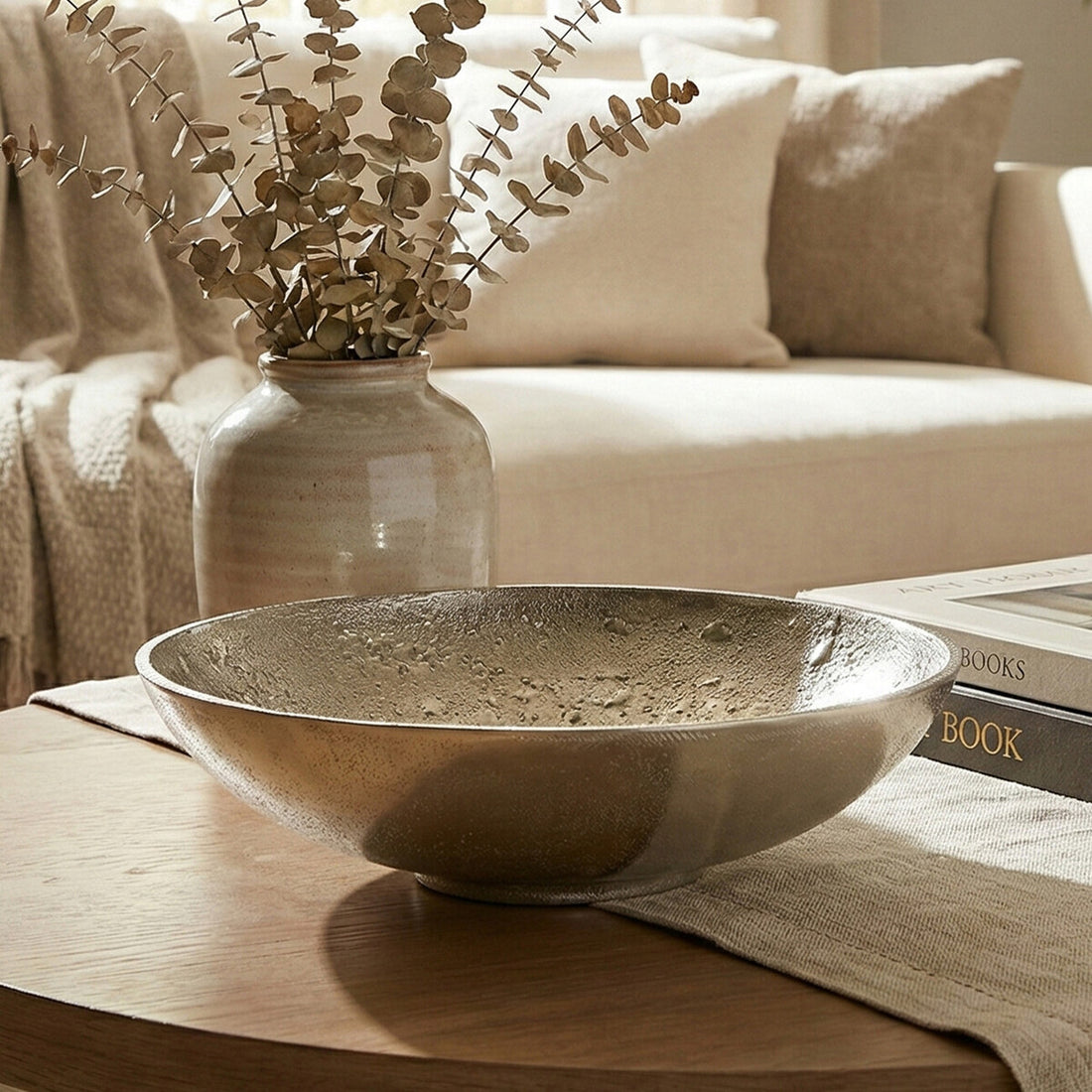 Decorative bowl on a coffee table with a vase of dried eucalyptus and books in the background.