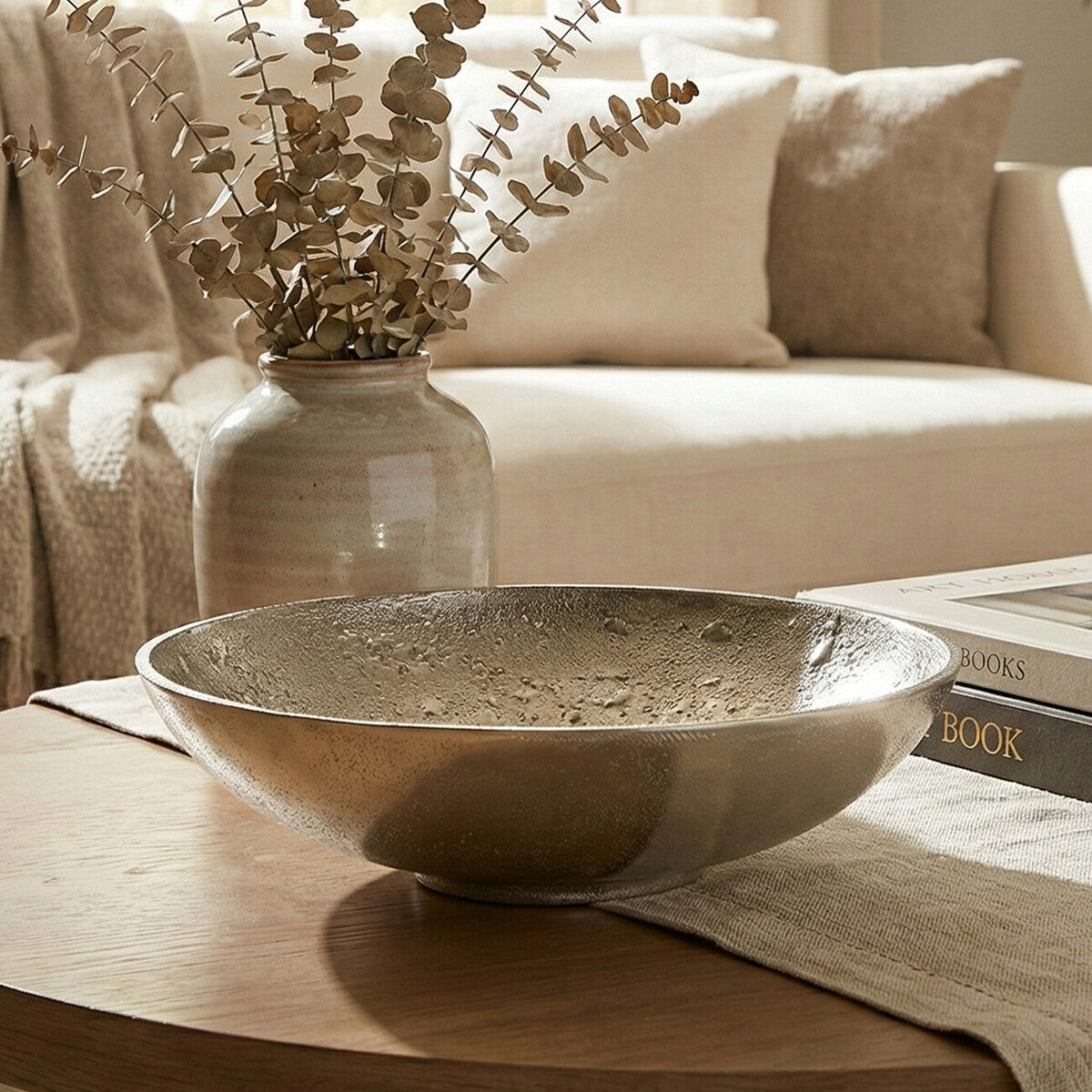 Decorative bowl on a coffee table with a vase of dried eucalyptus and books in the background.