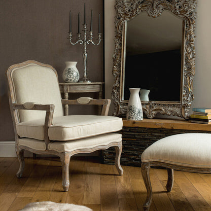 Living room with ornate mirror, chair, and ottoman on wooden floor.