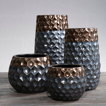 Set of four textured metal vases on a wooden surface with a gray background
