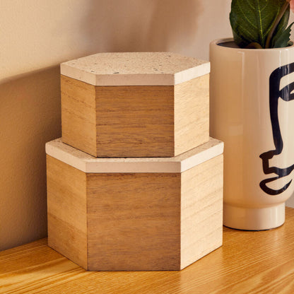 Two wooden hexagonal boxes stacked on a wooden surface with a vase containing pink flowers in the background.