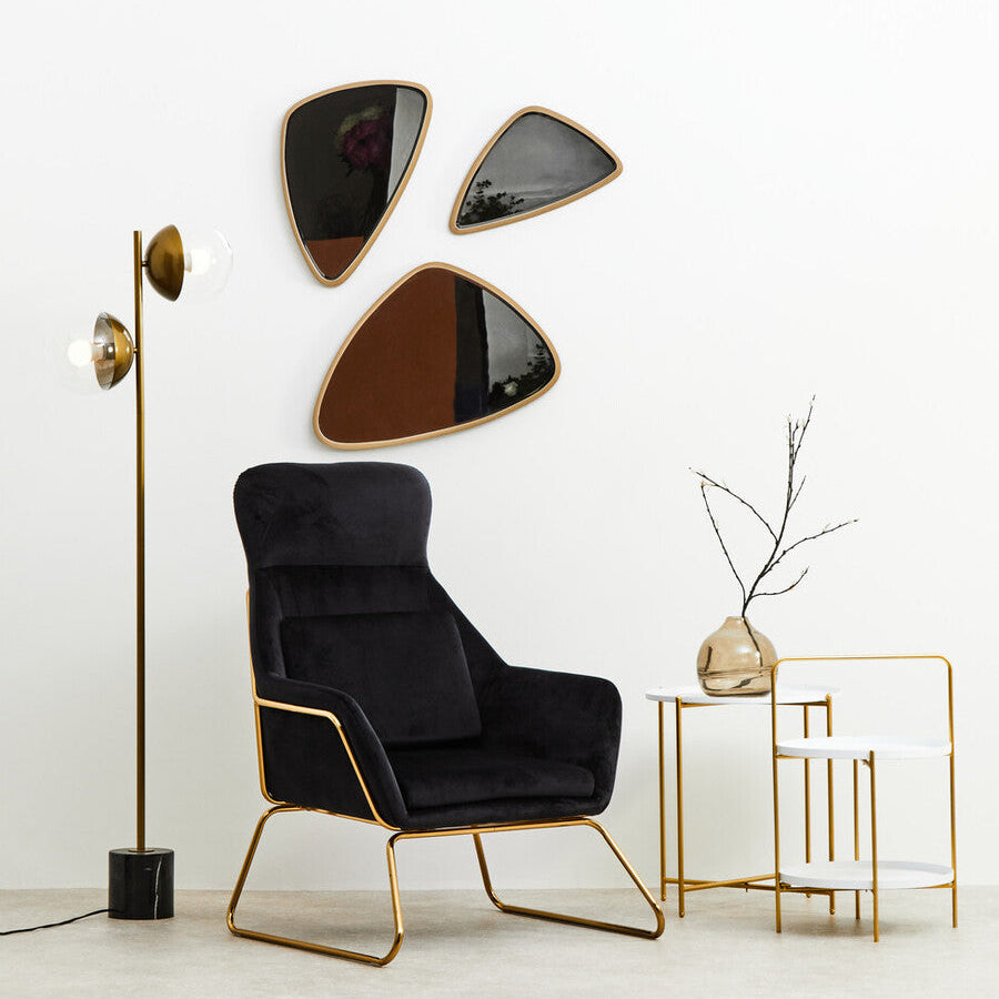 Modern black armchair with gold legs in a minimalistic room with wall art and side table.