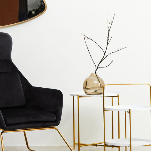 Modern black armchair with gold legs in a minimalistic room with wall art and side table.