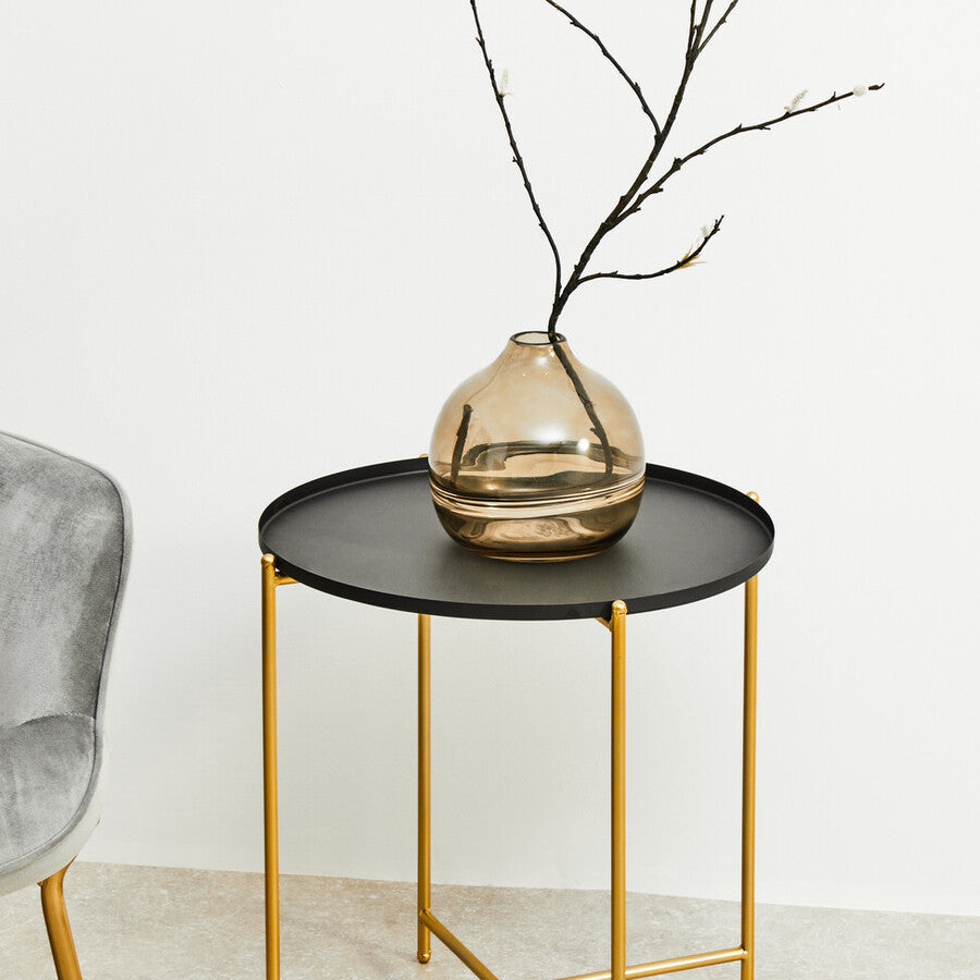 Small black side table with gold legs holding a vase on a light background