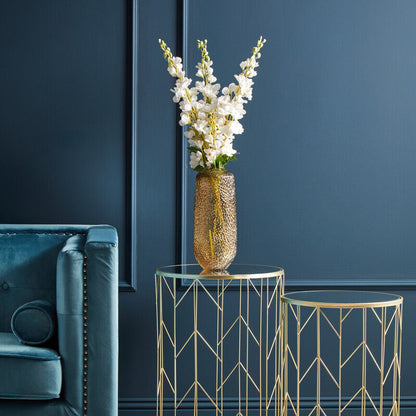 Gold side table with a vase of white flowers against a dark blue wall.