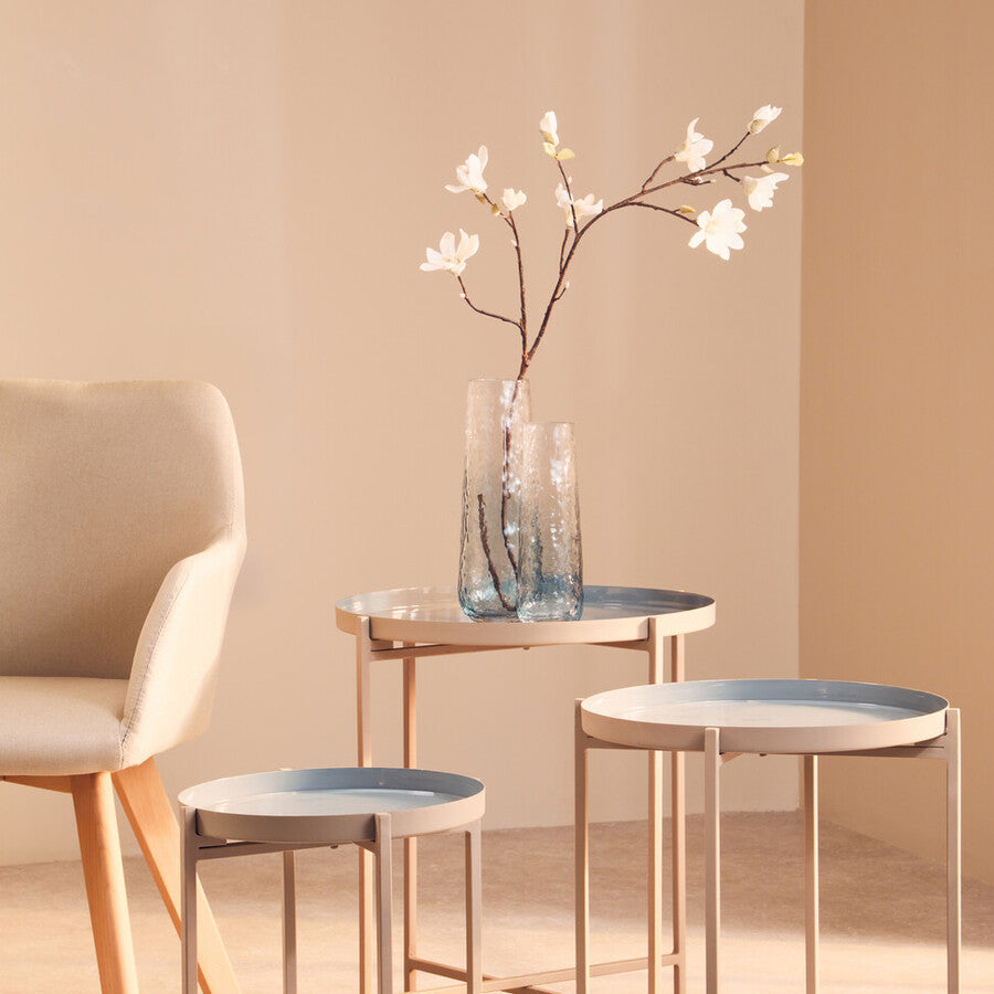 Set of three small tables with a vase of flowers on a beige background