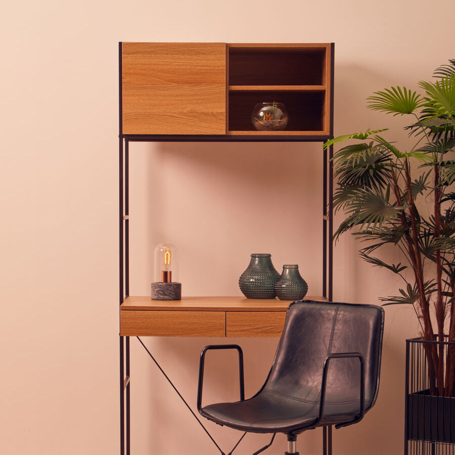 Wooden desk with shelves, black chair, and decorative items against a pink wall.