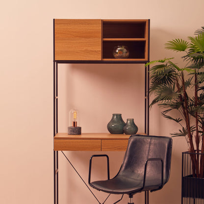 Wooden desk with shelves, black chair, and decorative items against a pink wall.