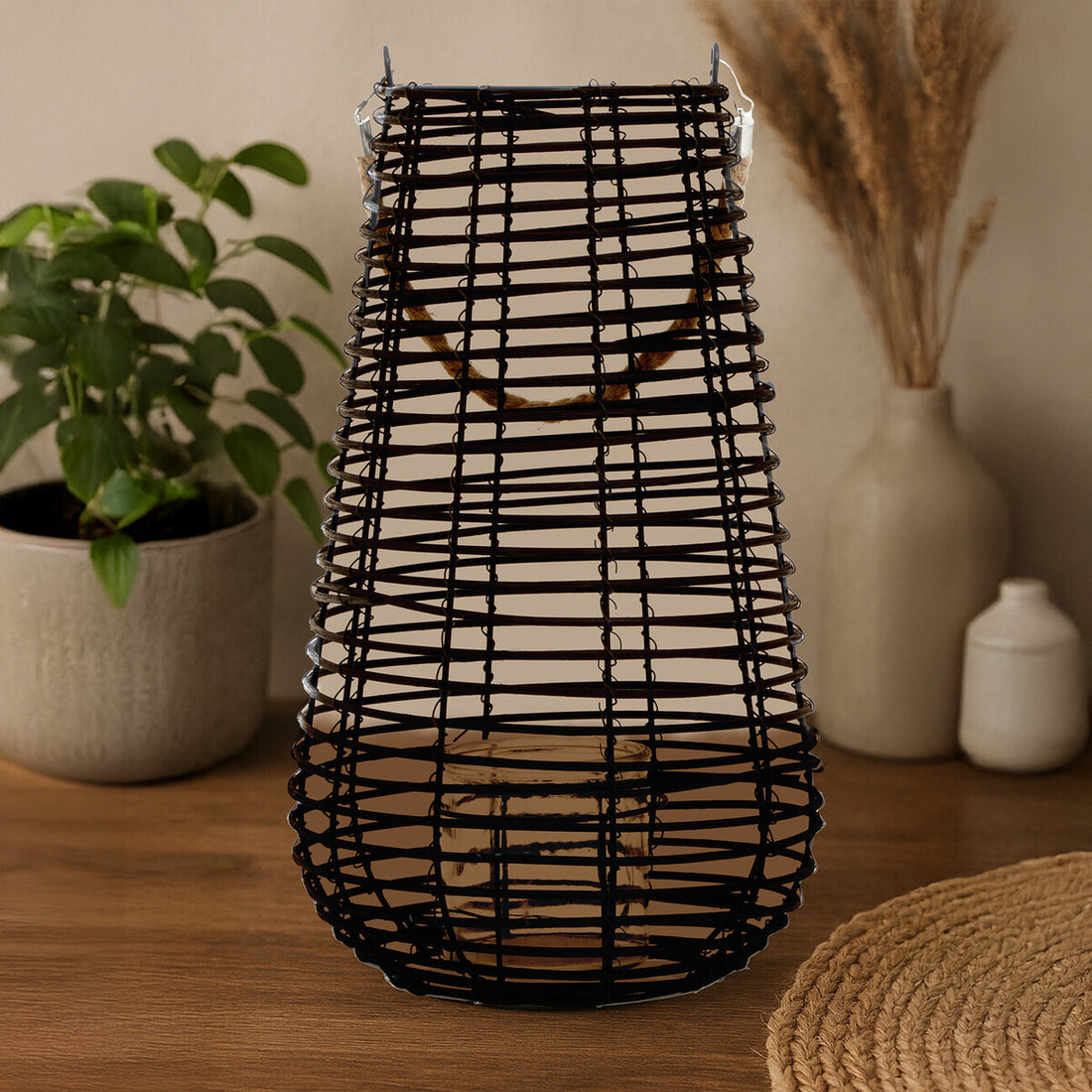 Black woven vase on a wooden surface with decorative items in the background