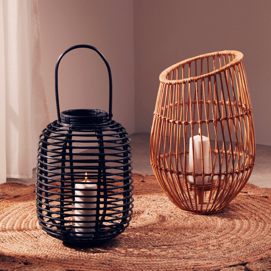 Two woven lanterns, one black and one brown, with candles inside on a wooden surface.