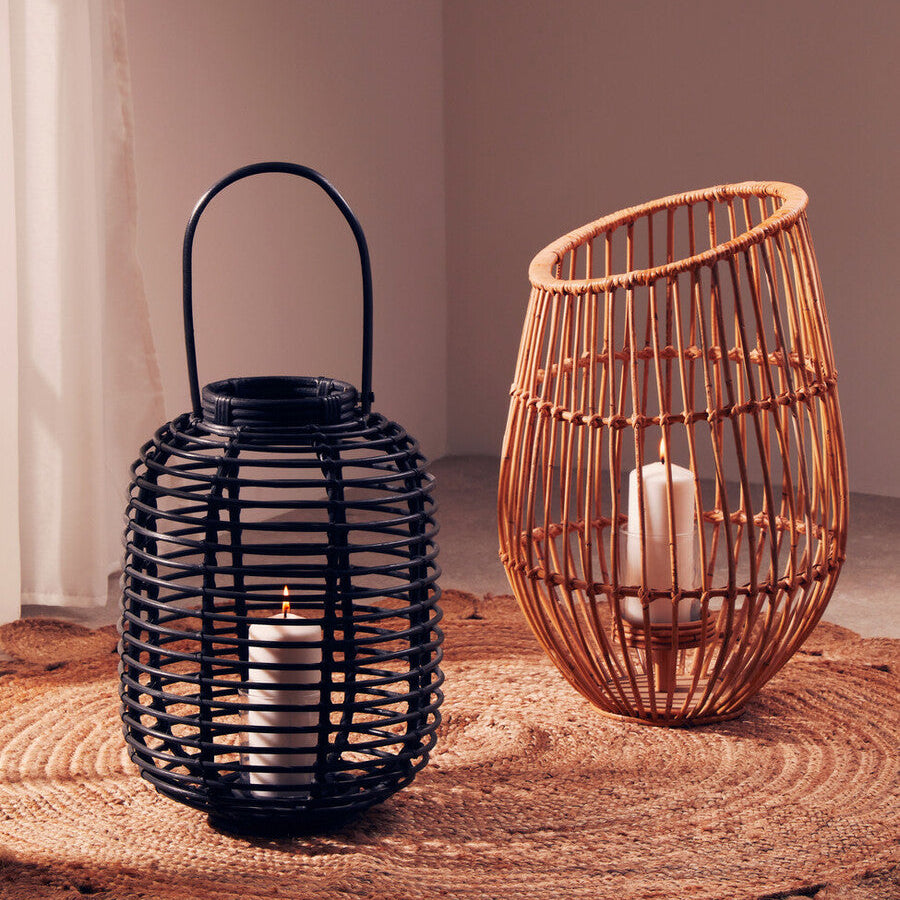 Two woven lanterns, one black and one brown, with candles inside on a wooden surface.