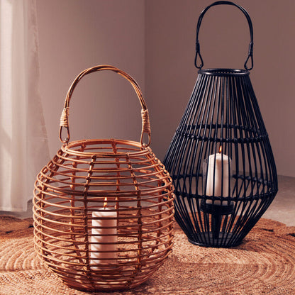 Two lanterns, one woven and one metal, with candles inside on a textured surface.