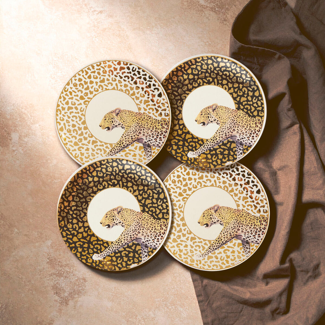 Four decorative plates with leopard designs on a textured surface.