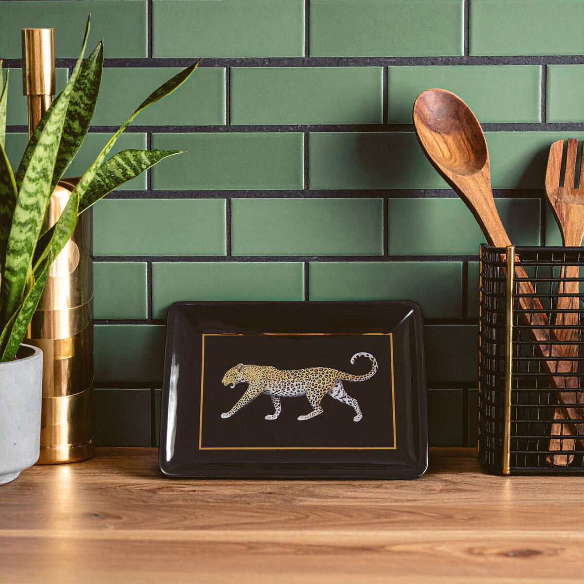 Decorative tray with a leopard design on a wooden surface against a green tiled wall.