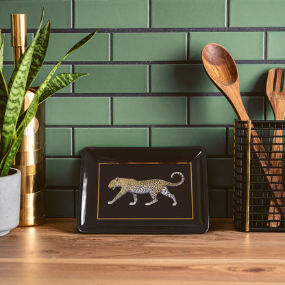 Decorative tray with a leopard design on a wooden surface against a green tiled wall.