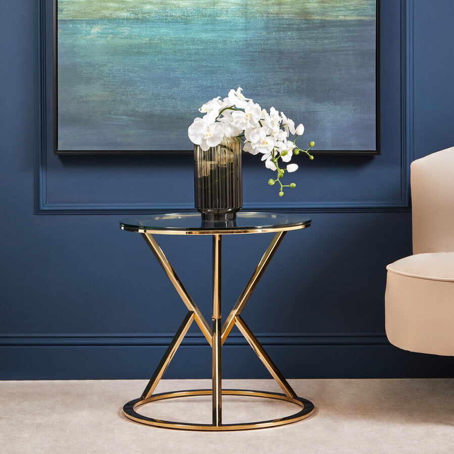 Gold side table with a vase of white flowers against a blue wall with abstract art.
