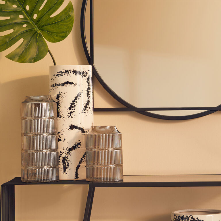 Decorative vases and a mirror on a shelf against a beige wall.