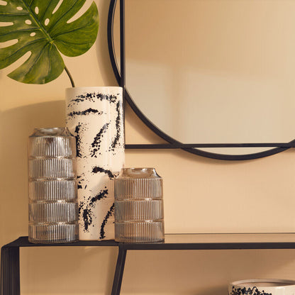 Decorative vases and a mirror on a shelf against a beige wall.