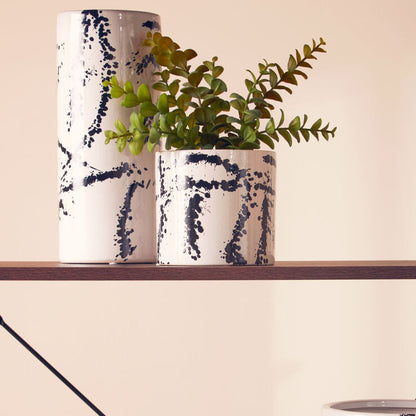 Decorative ceramic pots with black abstract patterns on a wooden shelf against a light wall.