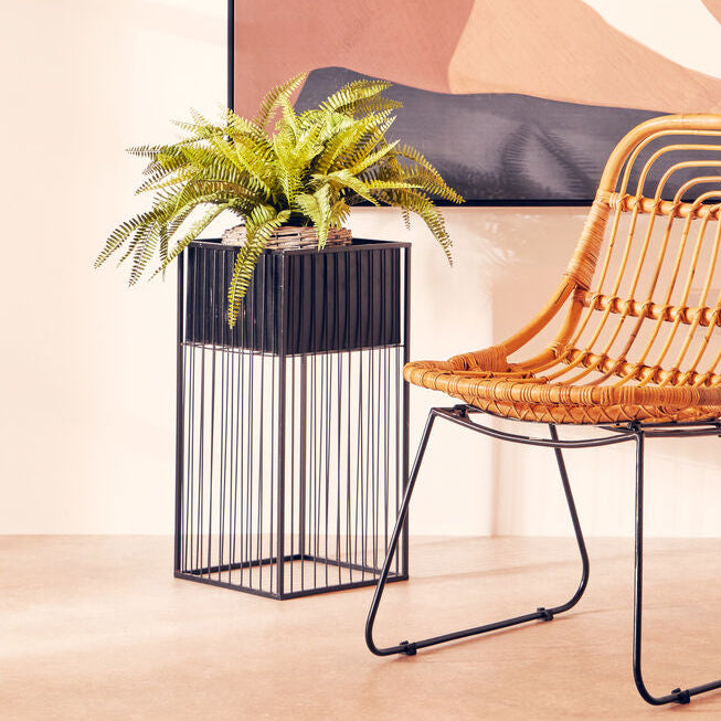 Wicker chair next to a plant in a decorative pot against a abstract wall art.