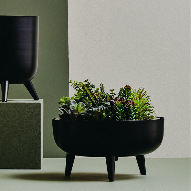 Two black planters, one with a plant, on a neutral background