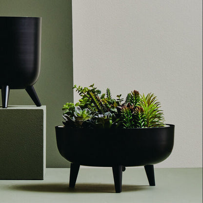 Two black planters, one with a plant, on a neutral background